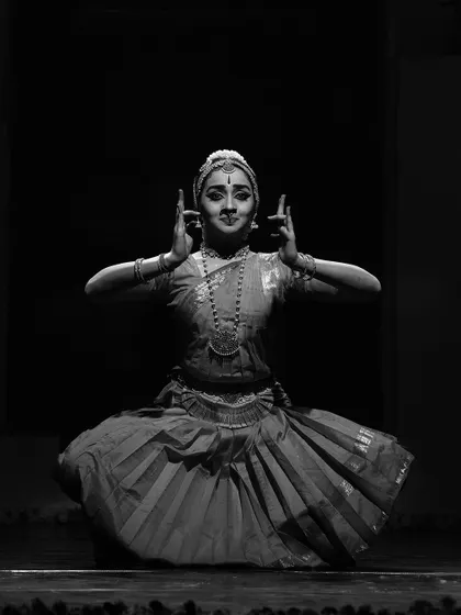 A black and white photograph of a classic seated pose, emphasizing the timeless geometry and grace of Bharatanatyam.