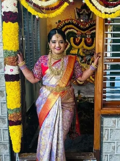 There is nothing more rewarding than seeing a happy bride on her special day. This client is glowing in her custom-designed silk saree and heavily embroidered blouse, standing in a beautifully decorated doorway during her ceremony.