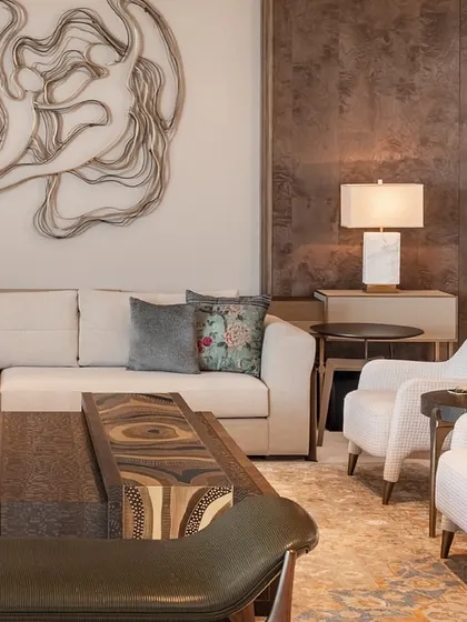 This angle highlights the relationship between the custom sofa, armchairs, and the striking metal wall art. The neutral color palette of the furniture allows the artwork to be the hero of the space.