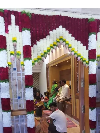 A housewarming ceremony in progress, with the main door decorated with intricate red and white flower garlands.