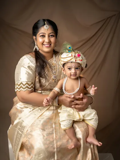 A mother holds her baby, both dressed in matching golden traditional wear for a Kannaiah-themed shoot. This portrait radiates warmth, love, and cultural pride.