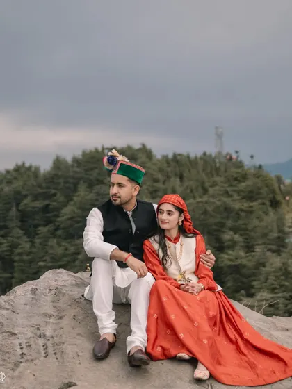 The couple sits together on a rock, looking out at the view. This shot captures a quiet, shared moment during their traditional Pahari pre-wedding shoot.