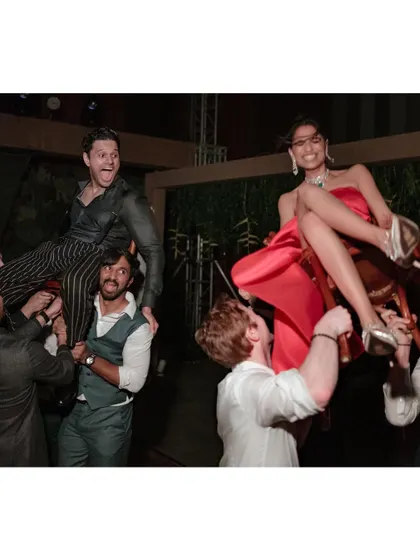 Saumya and Sid get lifted onto chairs at their after-party, a classic celebration moment. Their expressions of pure joy and the energy of their friends make this a fantastic party shot.