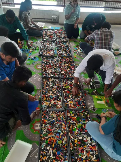 A wide view of a busy workshop in full swing. With trays full of LEGOs stretching across the floor, kids and adults get completely absorbed in the creative process.