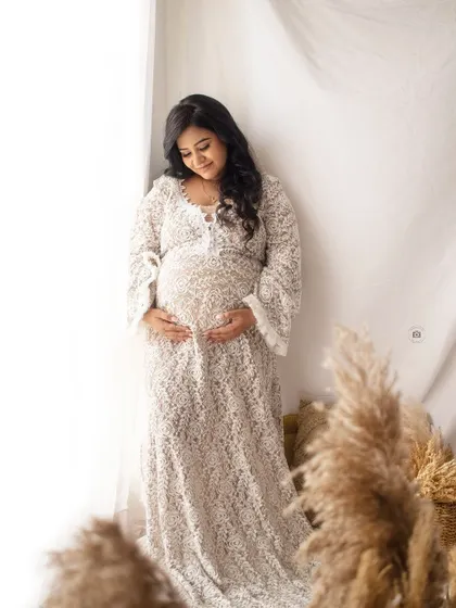 A serene solo portrait of a mother-to-be in a white lace gown, surrounded by soft light and boho decor.