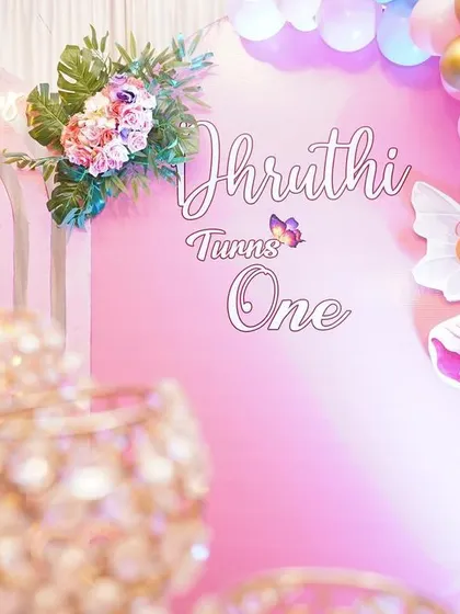 Detail shot of a first birthday backdrop, showing the combination of custom text, a fairy cutout, and a pastel balloon garland for a magical butterfly-themed party.