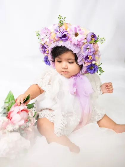 An eight-month-old baby curiously touches a bouquet of peonies during her floral-themed milestone photoshoot.