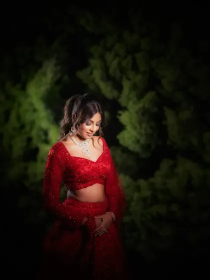 A portrait of the bride in a vibrant red reception outfit. The dark, natural background makes her and the color of her dress stand out beautifully.