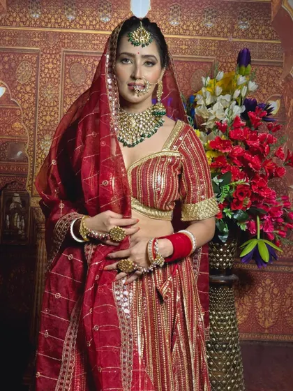 A full-length view of a bride in a traditional red outfit, wearing a custom green-beaded Kundan necklace set. This shows how the jewellery completes the entire bridal look.
