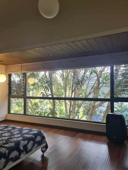 This bedroom is designed to feel like a treehouse, with a wall-to-wall window that offers an immersive view of the surrounding mango trees. The wood floor and ceiling enhance the natural, earthy ambiance.