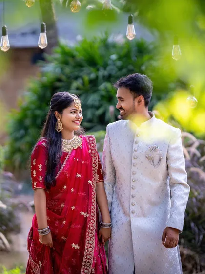 A sweet moment between a couple in traditional wear, framed by hanging lights and greenery.