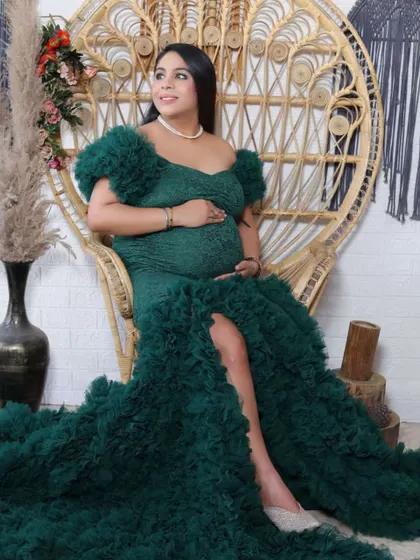 A confident pose from a mother-to-be in a stunning green ruffled gown, seated on an elegant peacock chair in our studio.