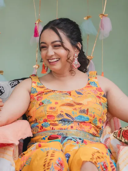 A joyful, laughing shot of the bride at her Mehendi. The vibrant yellow outfit is perfectly complemented by the all-pink makeup look, creating a fun and festive style.