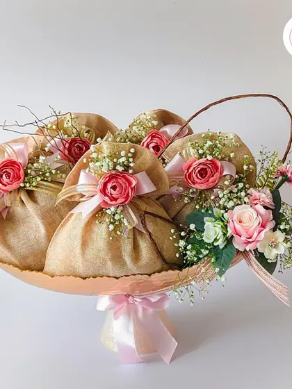 A beautiful arrangement of traditional dry fruit potlis in a decorative tray, adorned with pink flowers. A classic and elegant favor for any wedding function.