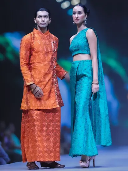 A slightly different pose from the same designer collection, this shot emphasizes the modern cut of the woman's top and the classic wrap of the man's tunic. It shows the blend of contemporary and traditional elements.