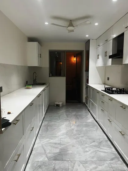 A full view of the parallel kitchen layout, which allows for an efficient work triangle between the stove, sink, and refrigerator. The grey marble-finish floor complements the white cabinetry.