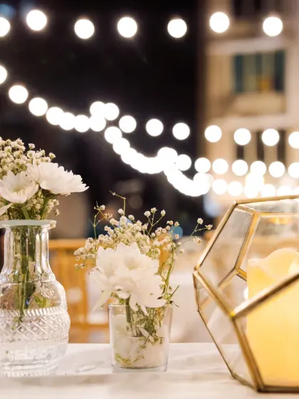 It's all about the ambiance. A close-up of the table decor, showing delicate baby's breath in vintage-style vases and geometric candle holders against a backdrop of twinkling lights.