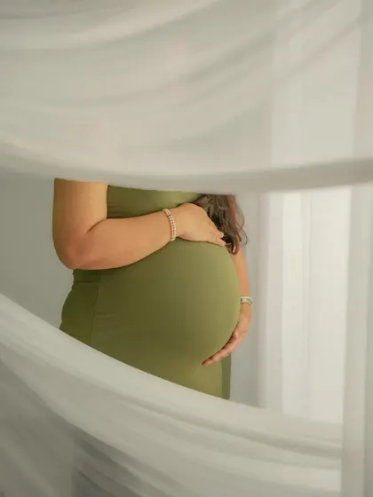 A close-up shot of the baby bump, framed by soft, sheer white curtains. This is a simple yet beautiful way to highlight the centerpiece of the maternity journey.