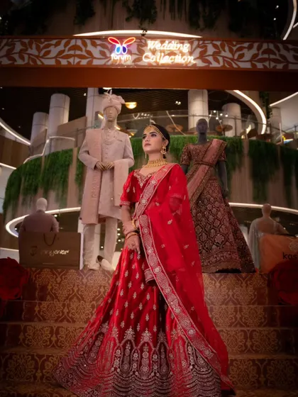 A grand, wide shot of a model in a red velvet bridal lehenga, standing on a staircase. A truly royal rental look.