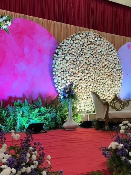 A modern and colorful stage with three large circular backdrops. The mix of a floral wall, a lit-up pink panel, and a blue panel creates a vibrant and artistic setting for a reception.