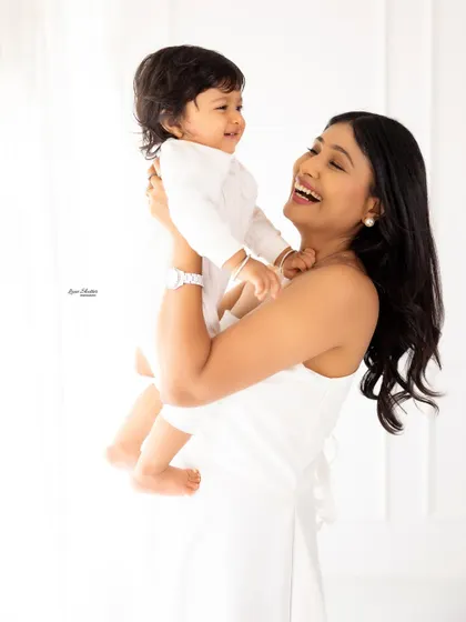 A mother lifting her baby up, both of them sharing a moment of pure joy and laughter. The bright, airy background adds to the lighthearted feel.