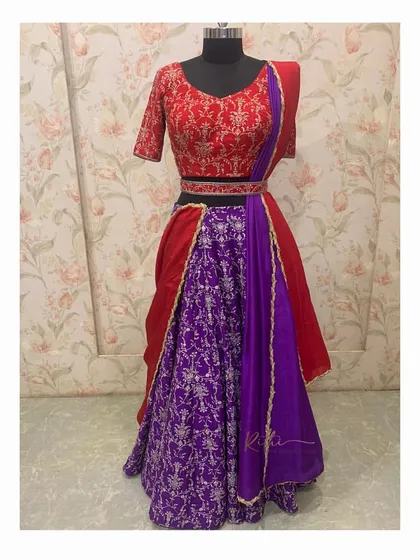 The full outfit on a mannequin, showing the red embroidered blouse, purple brocade skirt, and draped red and purple dupatta.