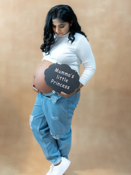 A casual and modern studio portrait of a mom-to-be cradling her bare bump, with a "Mumma's little Princess" sign.