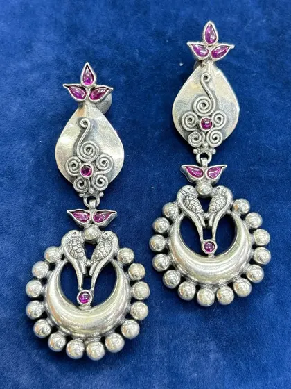 Pure silver chandelier earrings with a traditional design. This pair features intricate silver work with peacock motifs and pink stone accents, creating a beautiful dangling effect.