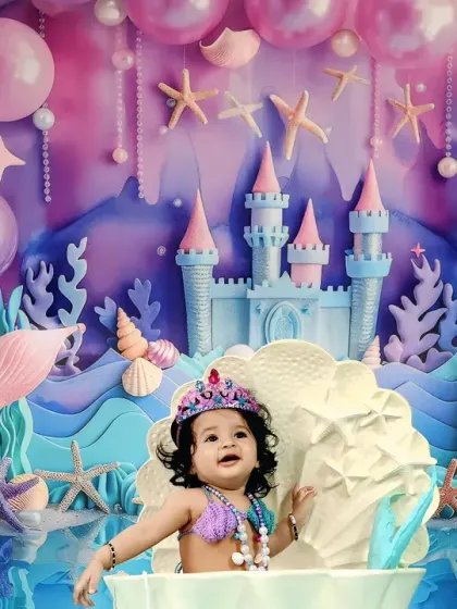 This little mermaid is having a blast, sitting in a giant clamshell with a joyful expression, surrounded by our magical underwater kingdom backdrop.