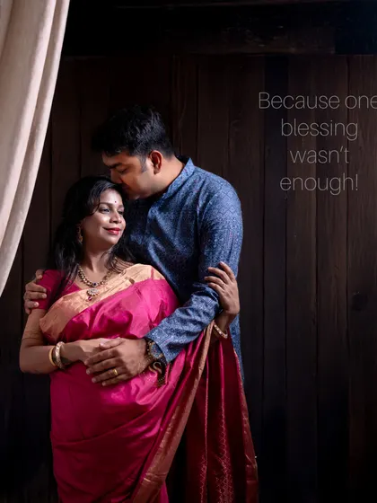 An emotional and intimate studio portrait of a couple celebrating their second pregnancy. The dark wood background adds warmth to the image.