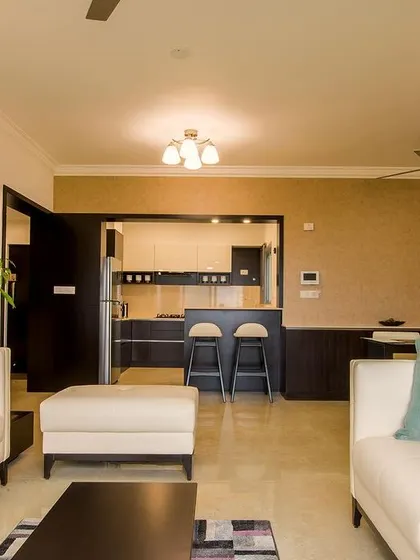 An open-concept living area where pops of purple and teal cushions add personality to neutral sofas, with a breakfast bar and kitchen visible in the background for a connected living experience.