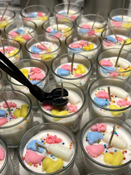 A close-up of me trimming the wicks on a batch of baby shower shot glass candles. Each candle is adorned with tiny wax baby feet, bottles, and ducks, making them adorable and memorable favors.