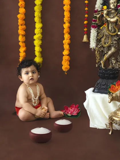 A simple and pure portrait of a baby dressed as Krishna against a clean brown backdrop.