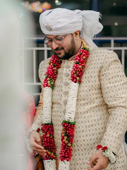 A portrait of the groom in his traditional sherwani and turban, looking down with a gentle smile. This is a classic groom portrait from the wedding day.