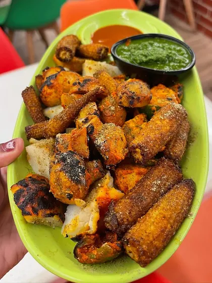 A vibrant shot of the All Mix Platter, featuring grilled paneer, baby corn, mushrooms, and potatoes, served with mint chutney and a tangy dip.