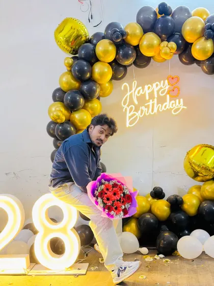 The birthday person posing with flowers in front of their 28th birthday balloon backdrop.