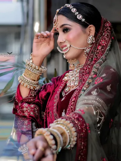 A side profile of the bride, highlighting her elaborate jewellery and the rich texture of her maroon velvet lehenga. The natural light beautifully illuminates her features.