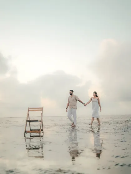 An artistic and minimalist shot of a couple walking on the beach. The empty chair adds a touch of surrealism and intrigue to this unique pre-wedding photo.