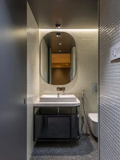 A compact powder room with an elegant oval mirror and white mosaic tiles, demonstrating our attention to detail in smaller spaces.