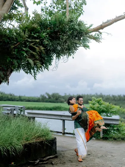 A joyful shot of the groom carrying his bride, with a beautiful natural backdrop, capturing a classic romantic pre-wedding pose.