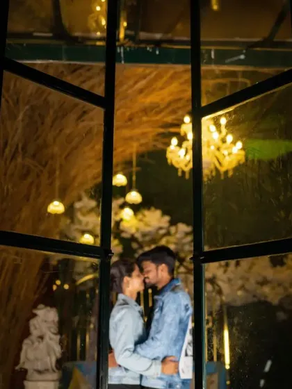A couple embraces behind a window frame at night, with chandeliers glowing in the background. This shot feels intimate and cinematic, like a scene from a movie.
