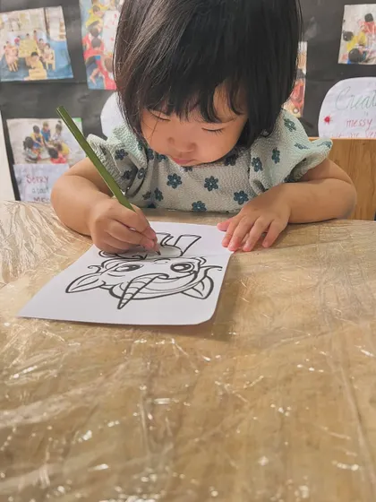 This toddler is deeply focused on her coloring sheet. Even simple scribbling is a crucial first step in the journey toward writing.