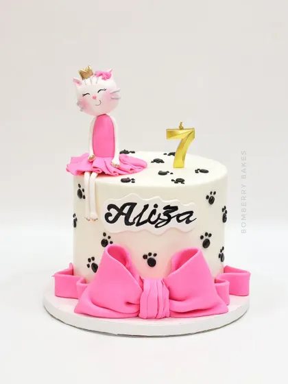 A sweet and simple cat-themed cake for a 7th birthday, featuring a cute kitty ballerina figurine and paw prints.