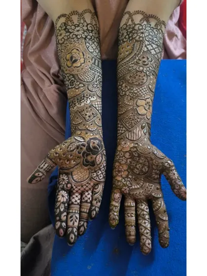 This design shows a classic combination of floral elements on the fingers and paisleys covering the arms, a hallmark of Indian bridal mehendi.