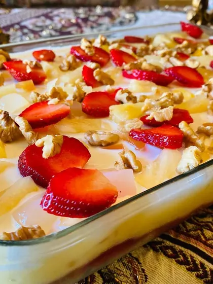 A beautiful fruit trifle with layers of custard, jam, cake, and topped with fresh strawberries and walnuts.