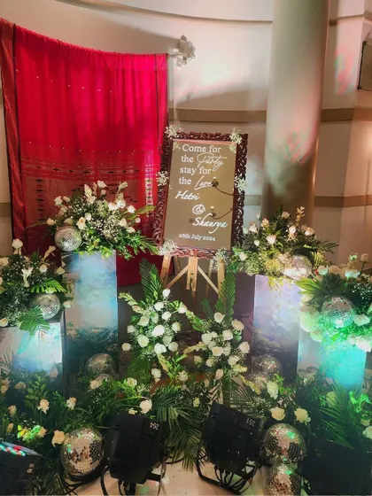 A creative welcome sign for a reception, surrounded by floral arrangements on illuminated pedestals and sparkling disco balls.