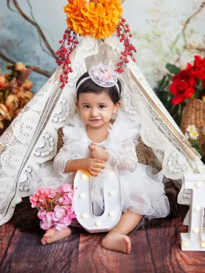 So much sweetness in one photo. This boho-chic teepee setup, surrounded by flowers, is perfect for a 'Wild One' or fairy garden theme. I love capturing these calm, classic portraits before the cake smash begins.