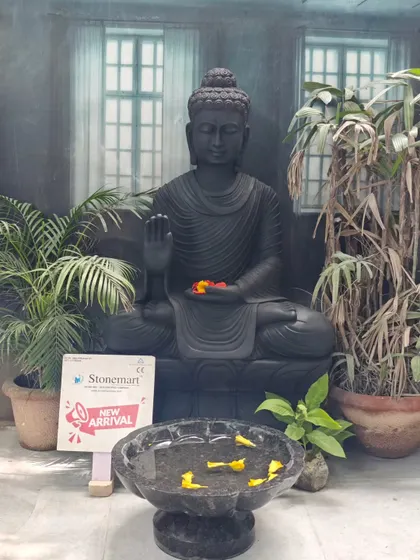 A full view of the 4-foot black marble Buddha statue with a floating flower bowl, set amongst plants to create a Zen garden feel.