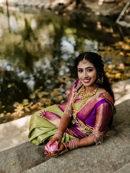 A smiling bride holding a lotus flower, sitting by the water. This serene and beautiful portrait captures a moment of peace and happiness.