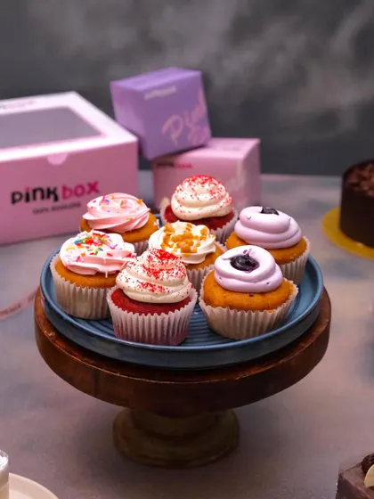 A beautiful display of our assorted cupcakes on a wooden stand. This shows the variety we offer, from Red Velvet and blueberry to caramel and strawberry.